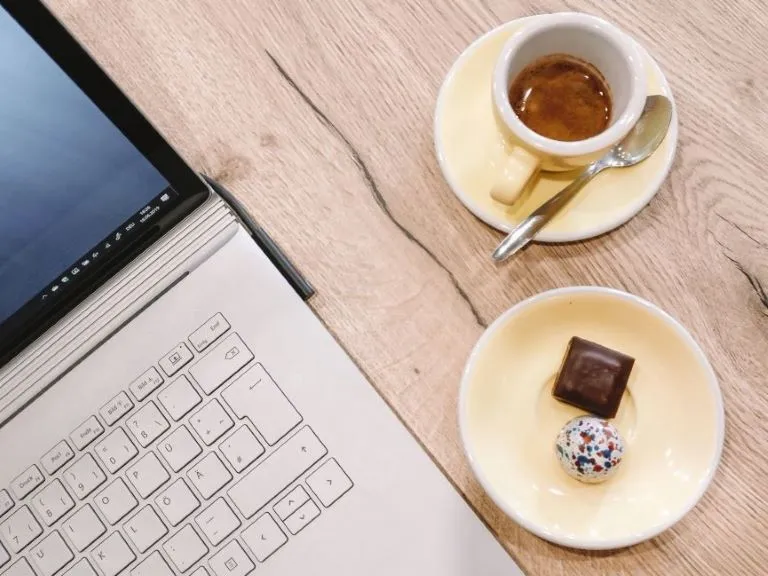 Top view of a table with a laptop and an espresso with pralines